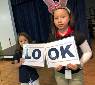 Two school girls holding the words LOOK on paper