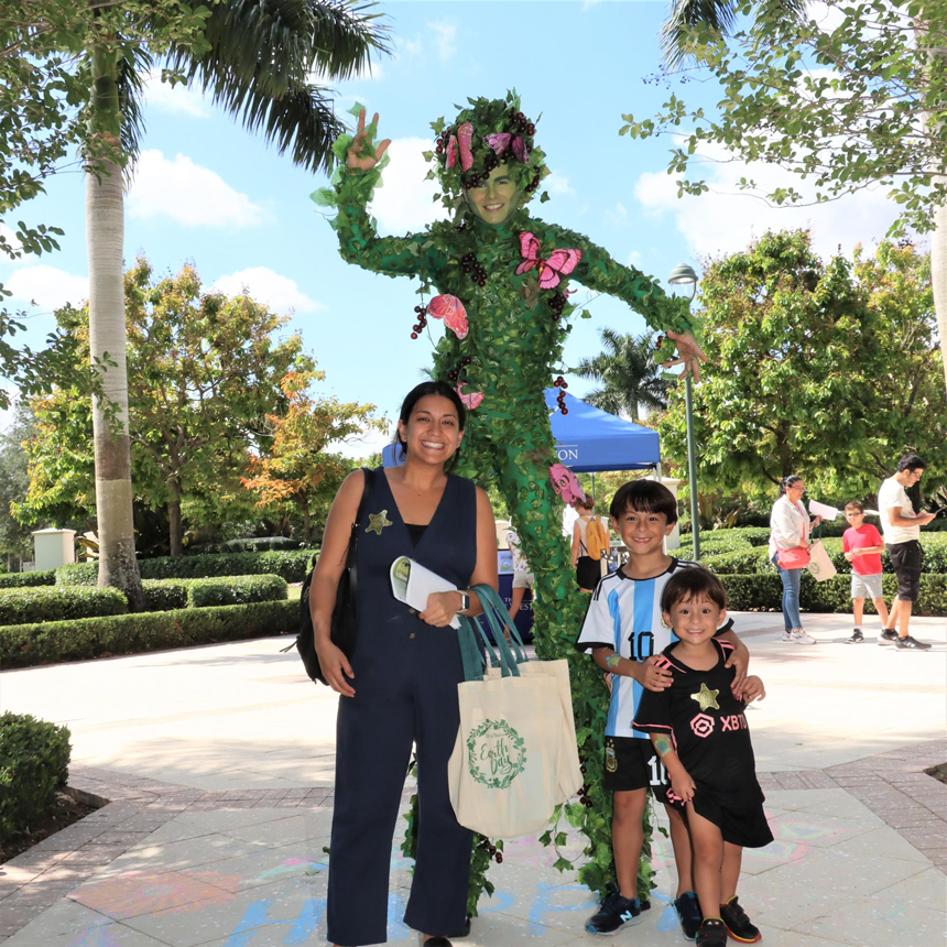 A mother and her two sons pose with the stiltwalker at the 2022 Earth Day event in Weston, Florida